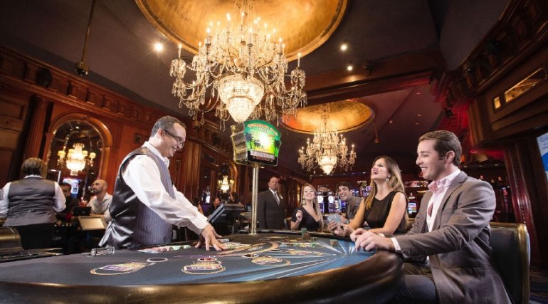 Зрелый мужчина крупье ведет игру в блэкджек для мужчины и женщины в роскошном казино